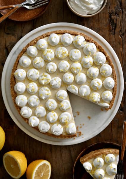 A top-down view of a cheesecake topped with dollops of whipped cream and lemon zest.