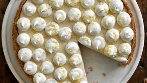 A top-down view of a cheesecake topped with dollops of whipped cream and lemon zest.