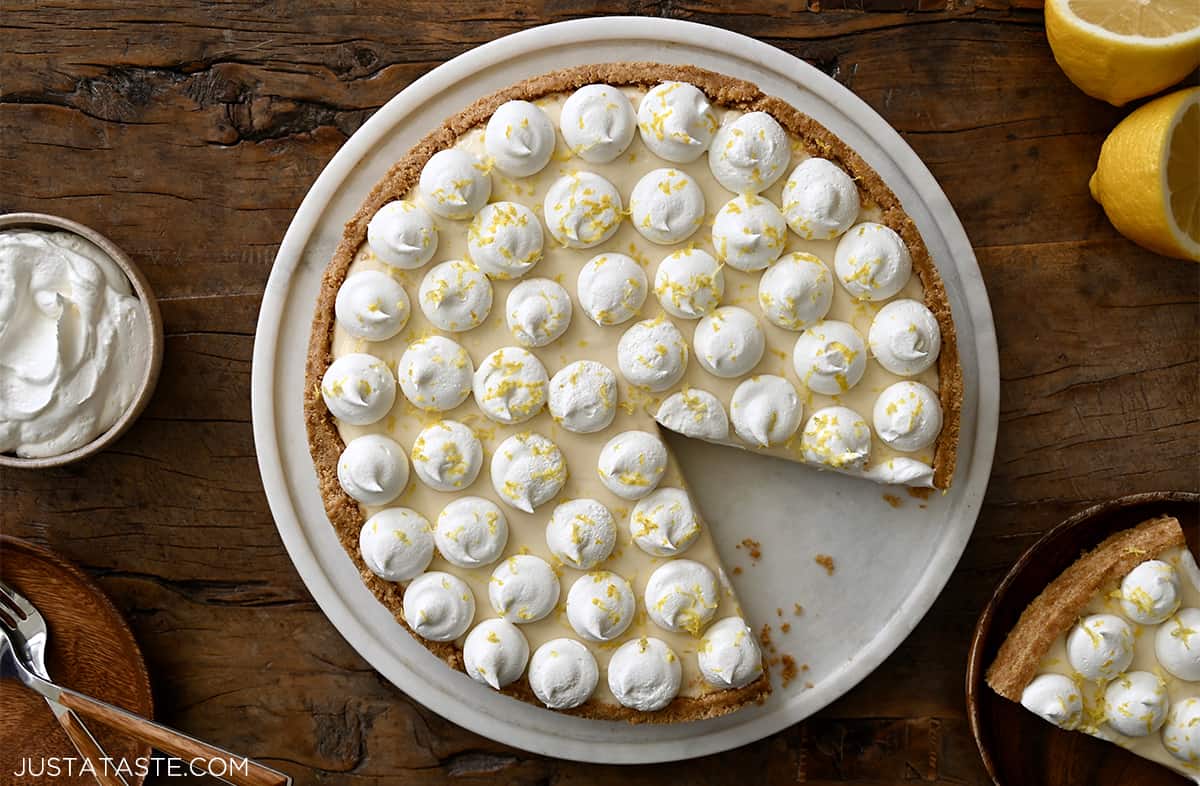 Dollops of whipped cream atop a cheesecake with a graham cracker crust on a round serving plate.