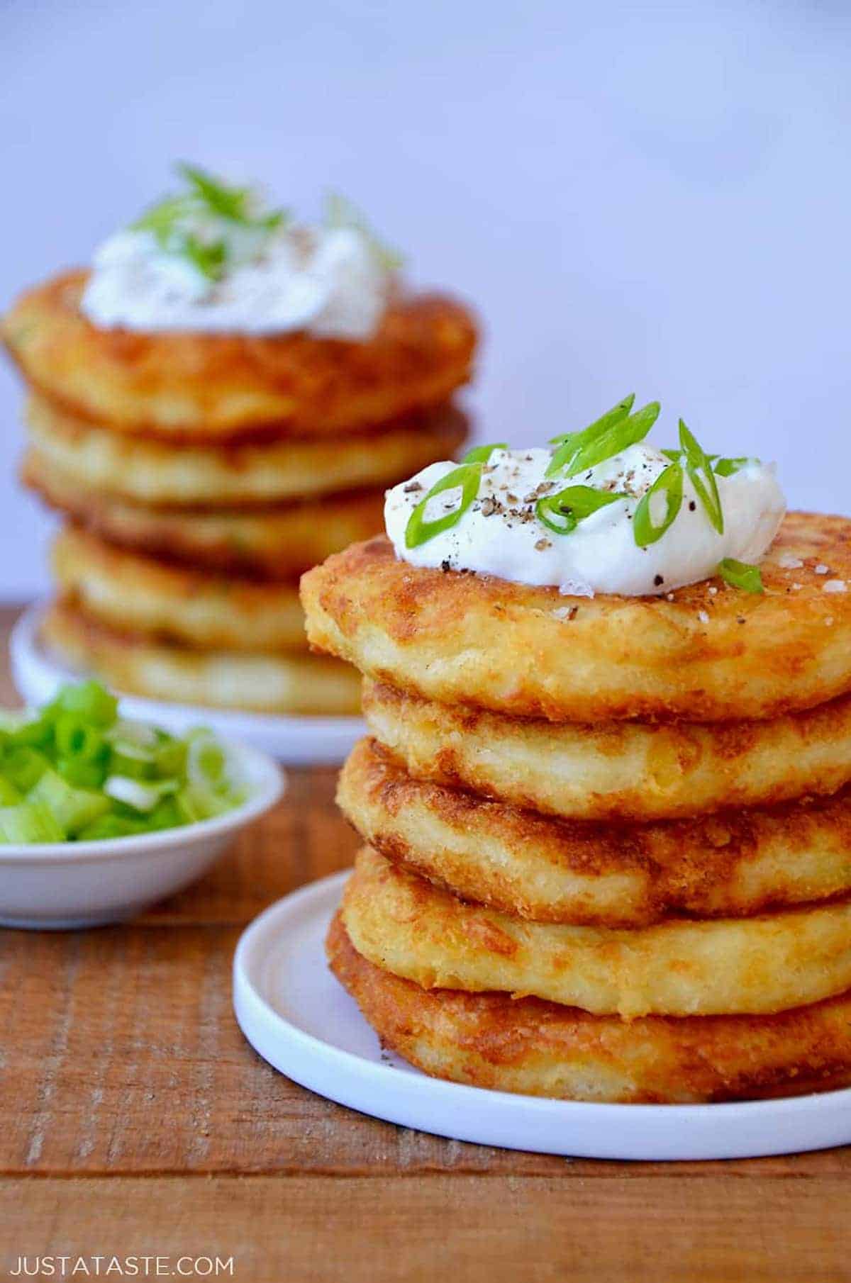 A stack of cheesy mashed potato pancakes topped with sour cream and chopped scallions.