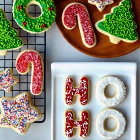 Sugar cookies with frosting and sprinkles on a wire cooling rack, on a plate and on a white serving platter.