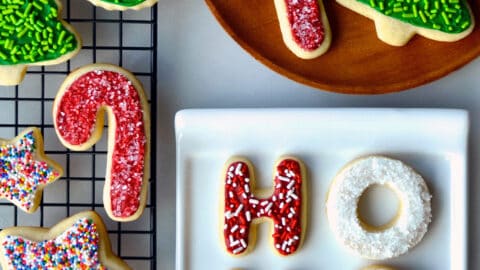 Sugar cookies with frosting and sprinkles on a wire cooling rack, on a plate and on a white serving platter.