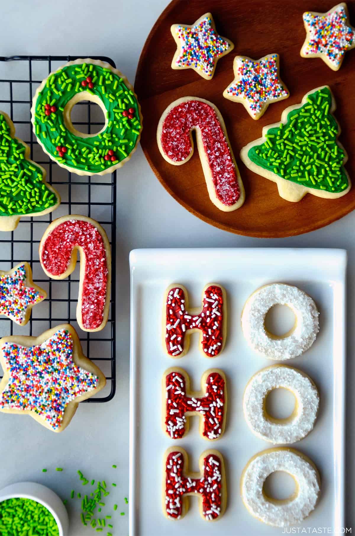 Sugar cookies with frosting and sprinkles on a wire cooling rack, on a plate and on a white serving platter.