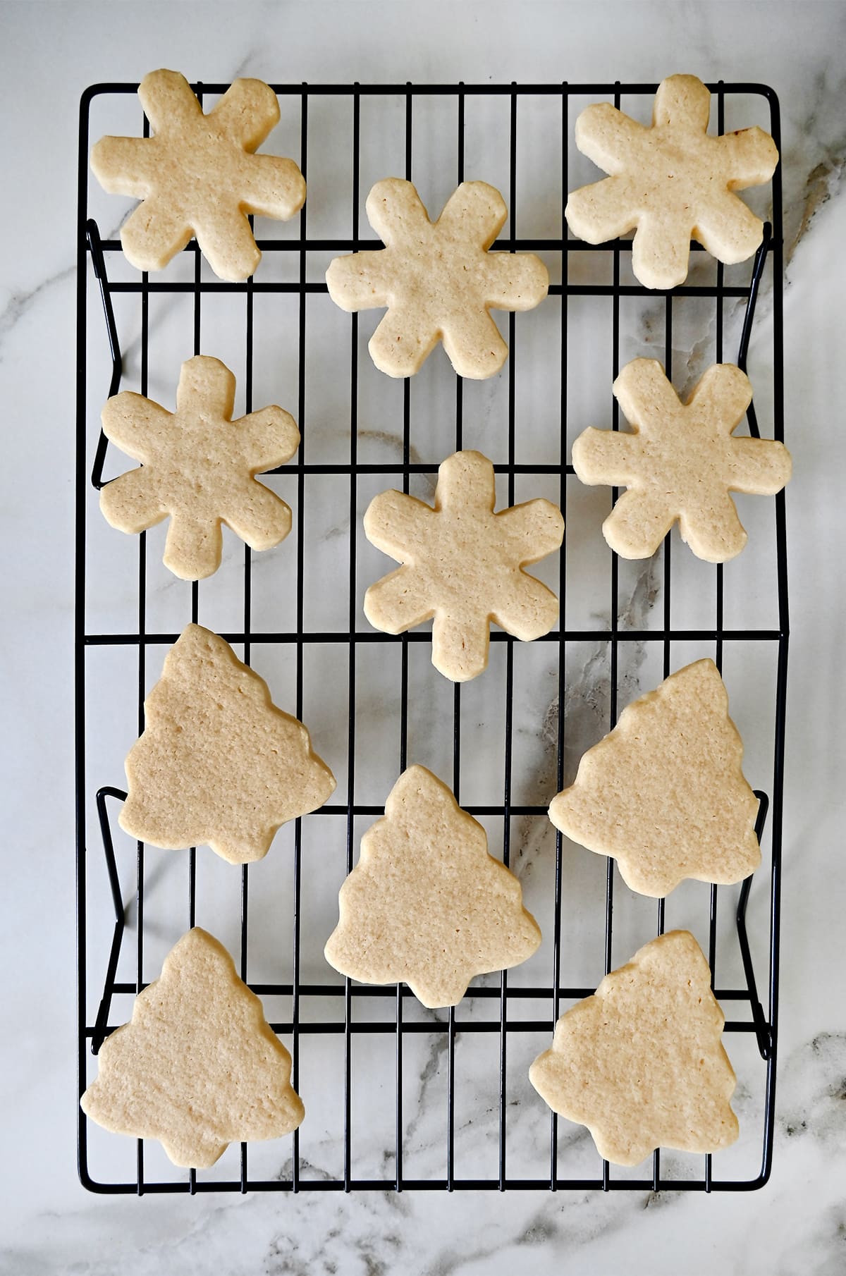 Sugar cookies in the shapes of Christmas trees and snowflakes cooling on a wire rack.