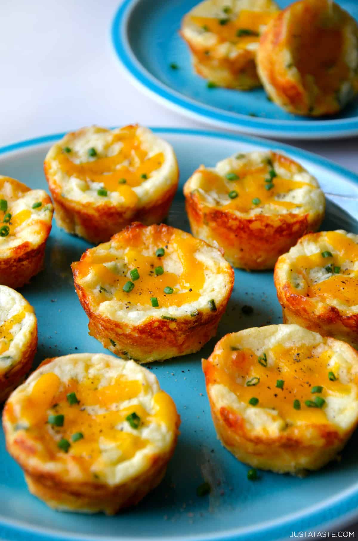 A blue plate with cheesy mashed potato muffins garnished with black pepper and chopped chives.