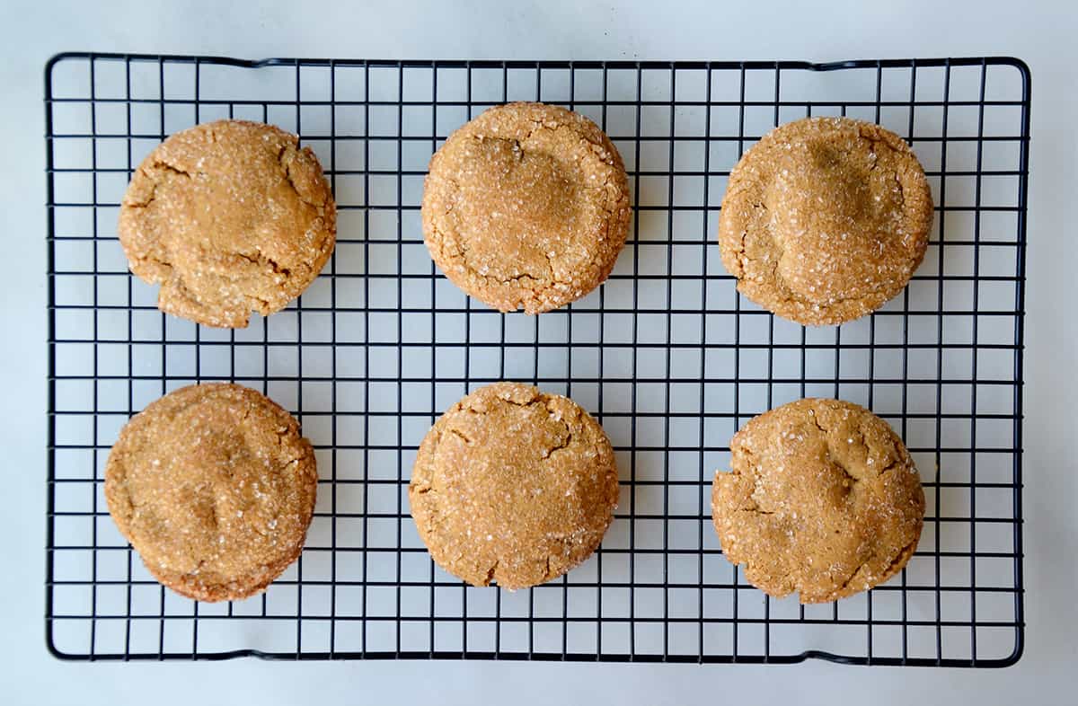 Baked ginger cookies sit on a wire cooling rack on the counter.