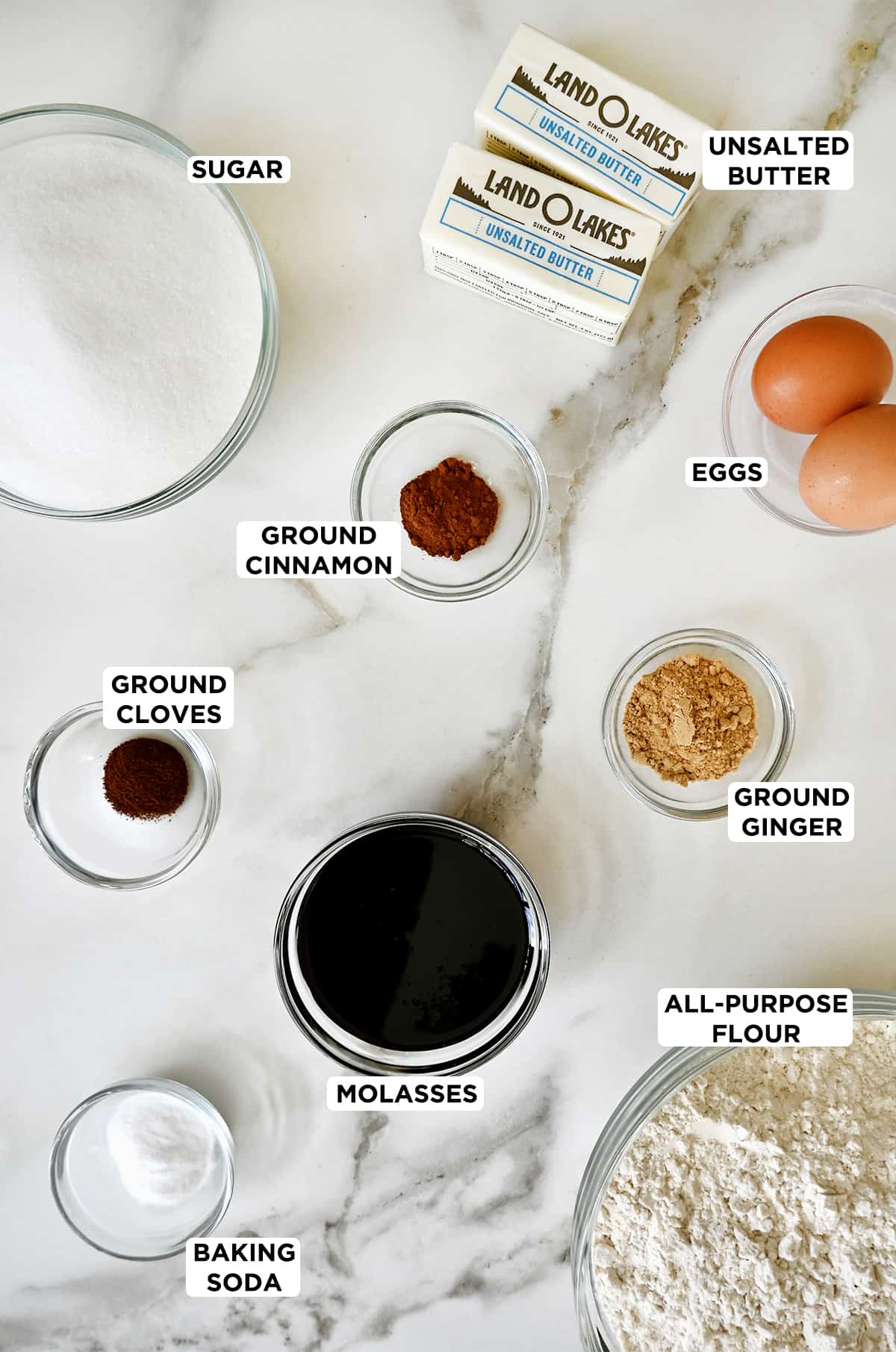 Ingredients for making ginger cookies are measured out into glass bowls, including spices, eggs, molasses, flour and sugar.