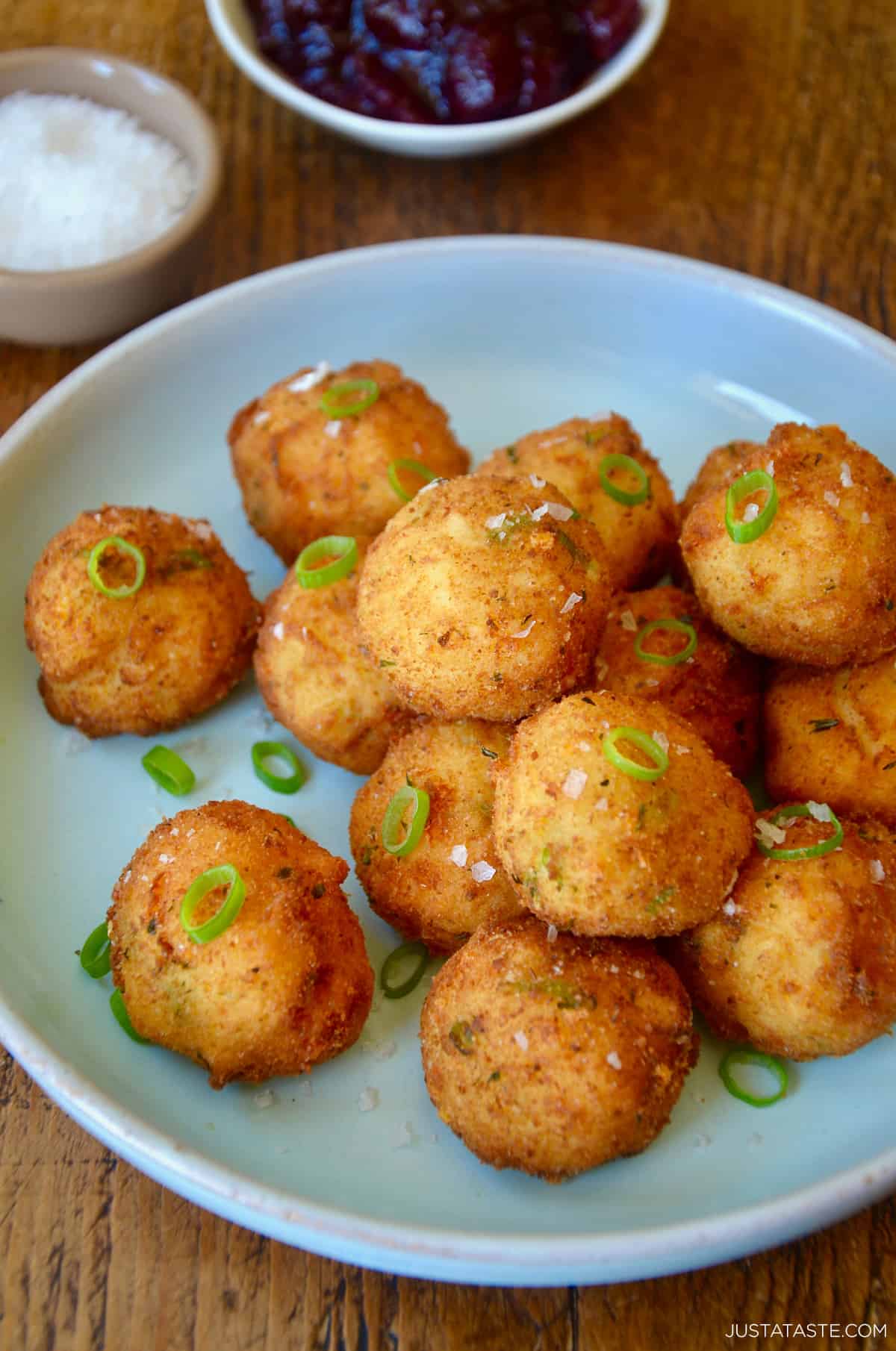 Crispy potato croquettes garnished with chopped scallions, salt and pepper on a blue plate.