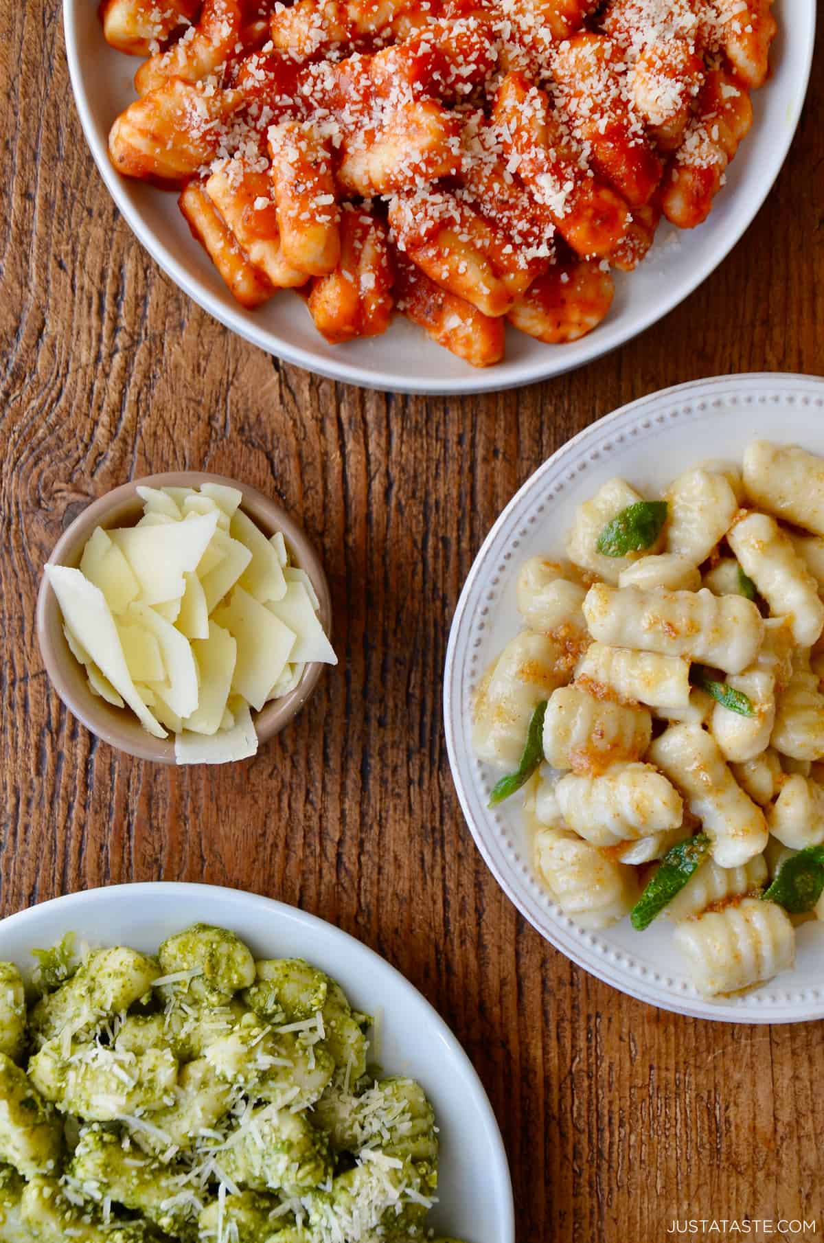 Three plates containing mashed potato gnocchi, one with tomato sauce, another with pesto and the third with crispy sage. 