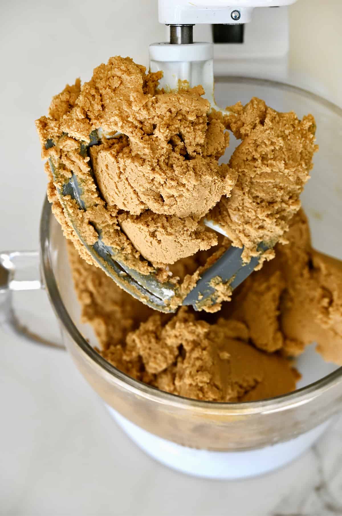 Ginger molasses cookie dough sits in the glass bowl of a stand mixer, ready to be shaped into balls.