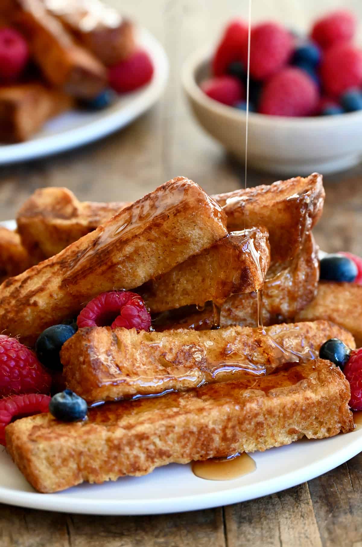 A pile of French toast sticks on a plate being drizzled with maple syrup.