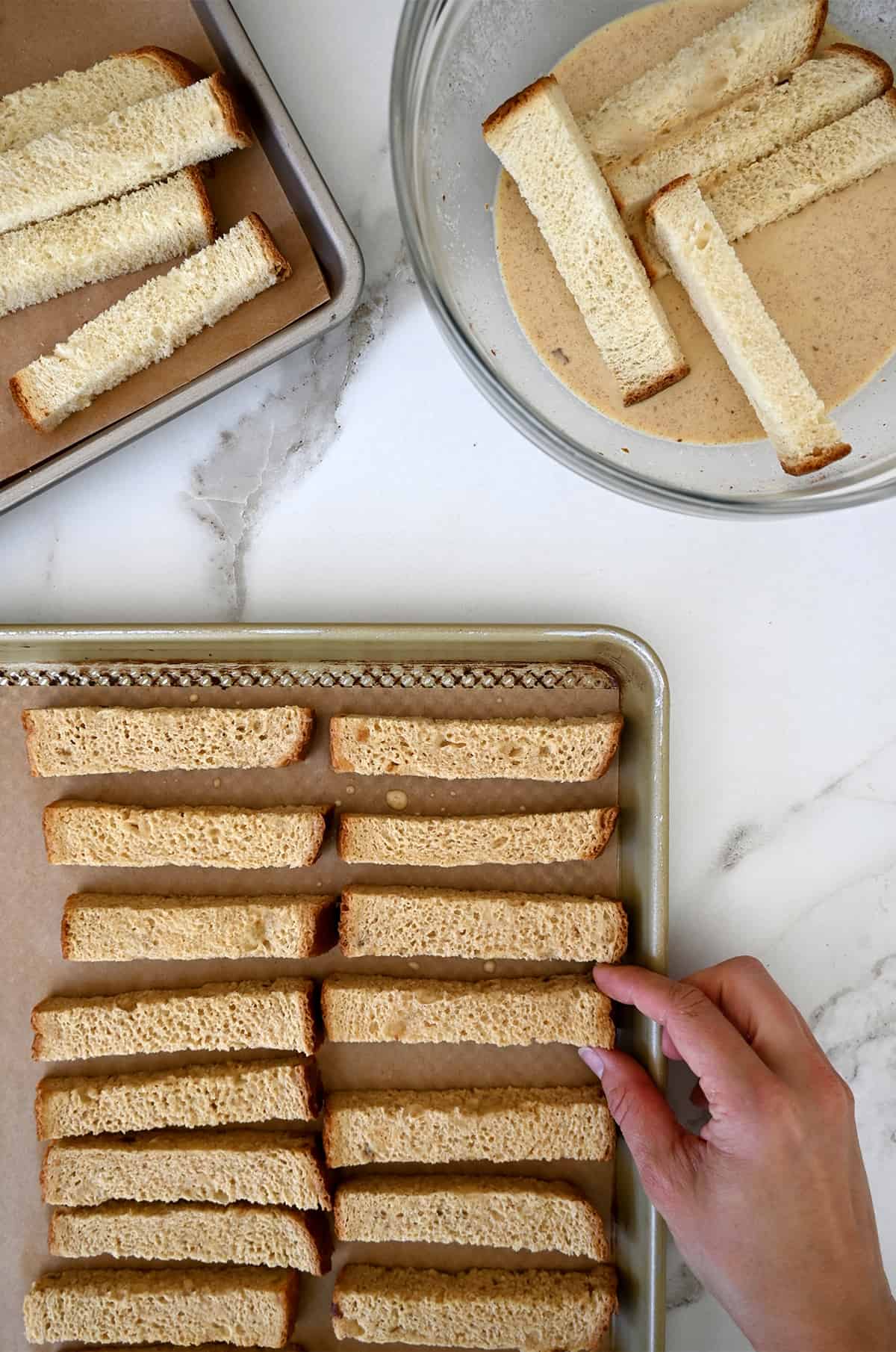 Bread sticks coated in a cinnamon-vanilla custard on a parchment-paper lined baking sheet.