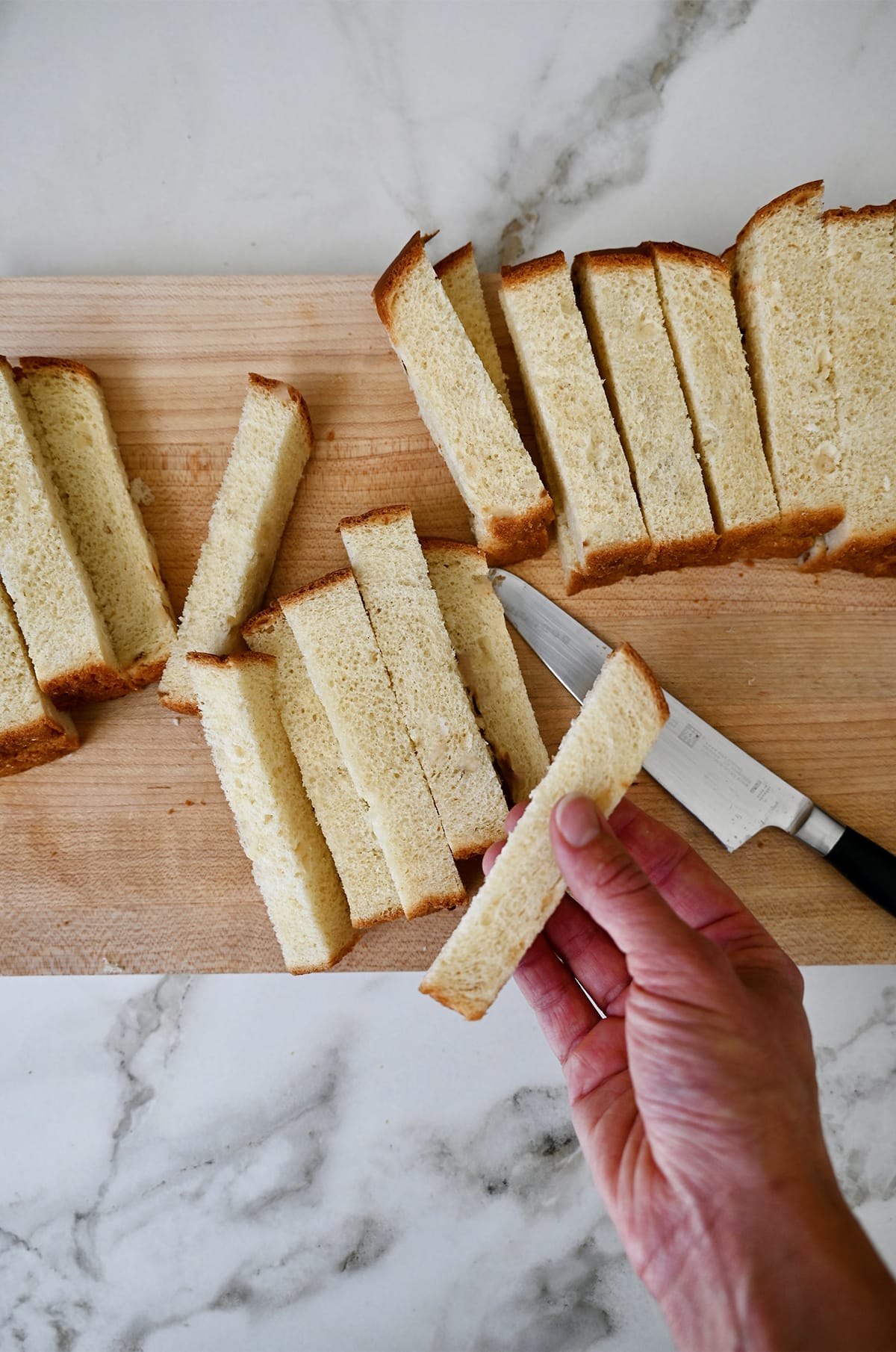 Slices of Texas toast on a cutting board with a hand holding one slice.