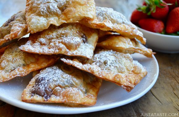 A white plate containing chocolate wontons covered with powdered sugar