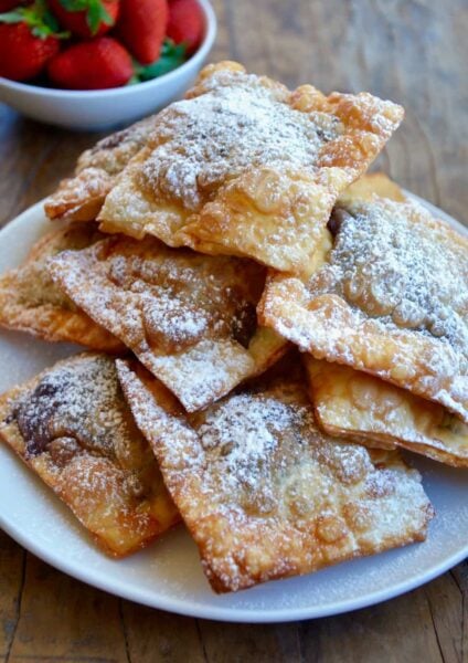 A white plate containing a pile of chocolate wontons covered with powdered sugar