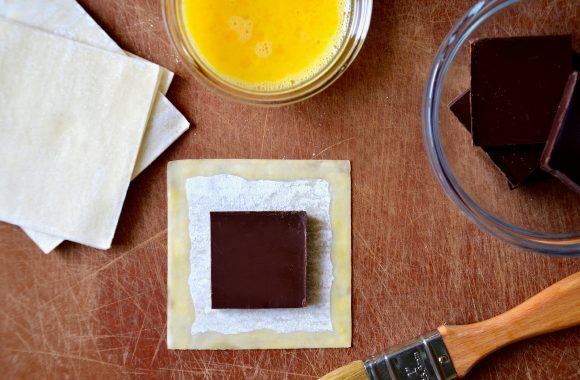 A cutting board with wonton wrappers, chocolate, an egg wash and a pastry brush