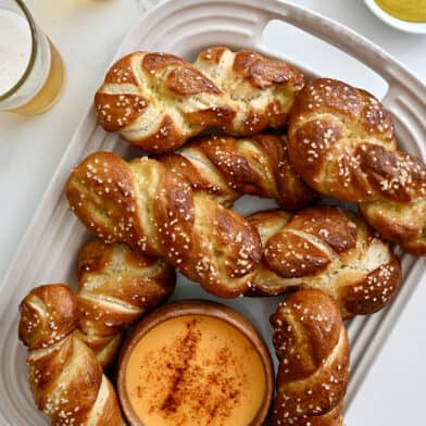 A top-down view of a serving platter containing soft pretzel twists and a small bowl containing beer cheese dip