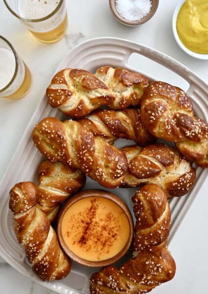 A top-down view of a serving platter containing soft pretzel twists and a small bowl containing beer cheese dip