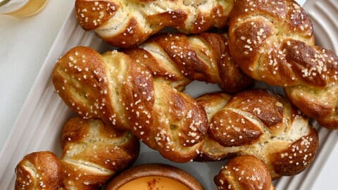 A top-down view of a serving platter containing soft pretzel twists and a small bowl containing beer cheese dip