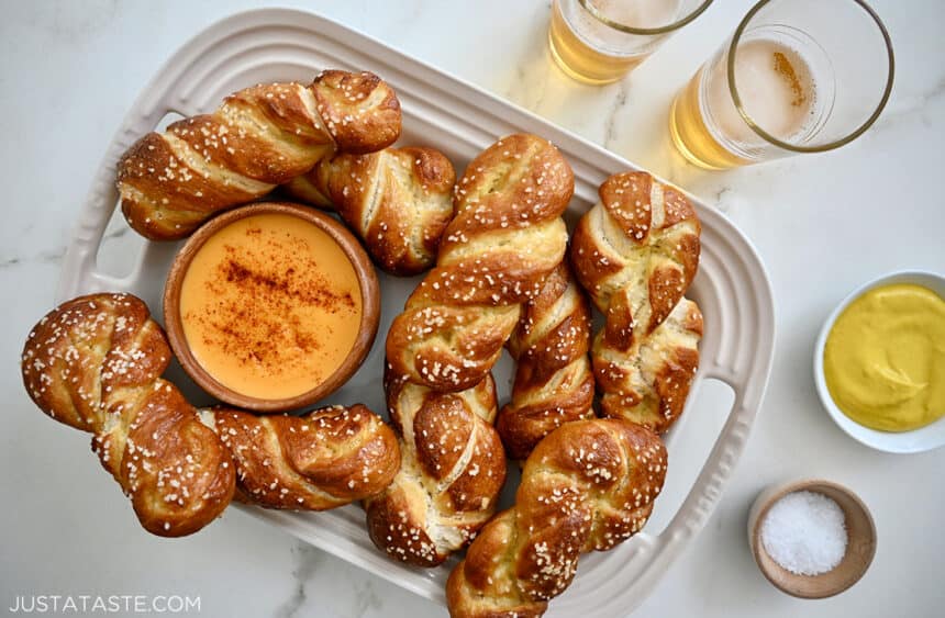 Easy homemade soft pretzel twists on a serving plate with a small bowl containing beer cheese dip next to two glasses filled with light beer