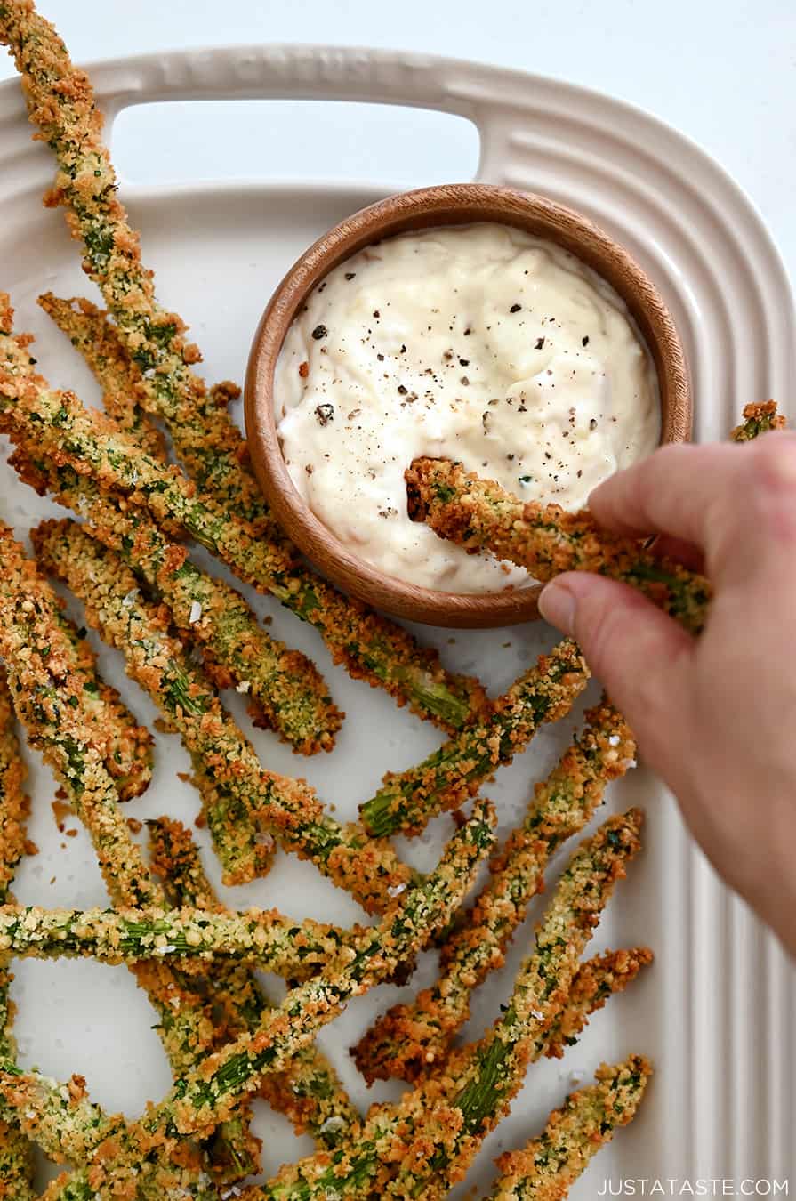 A hand dipping roasted asparagus fries into garlic aioli