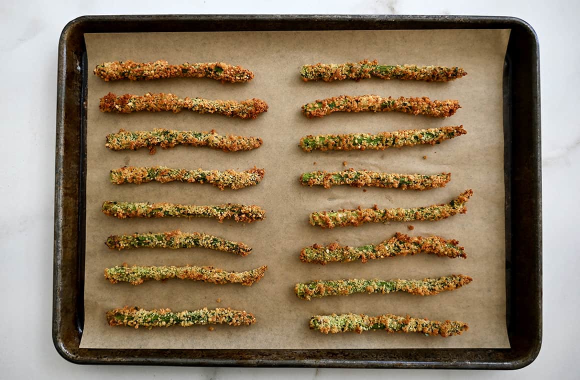 Oven roasted asparagus fries atop a parchment paper-lined baking sheet