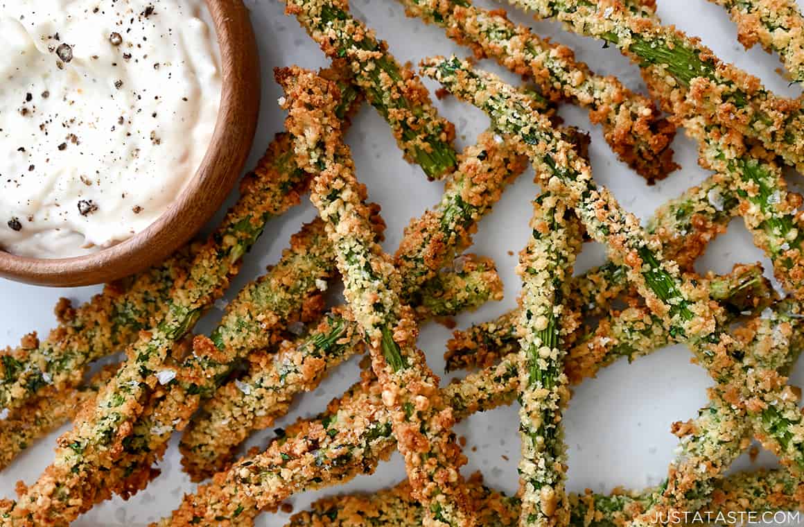 A close-up view of air fryer asparagus fries next to a small bowl containing roasted garlic aioli