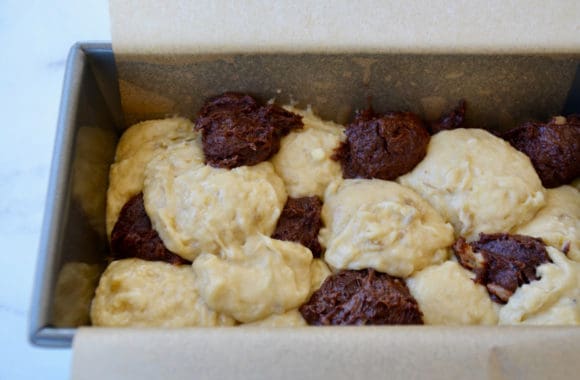 Parchment paper lined bread pan containing alternating banana batter and the chocolate batter