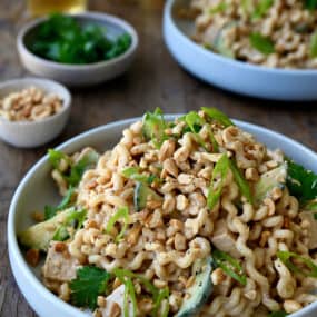 Thai Chicken Pasta Salad in a white bowl garnished with sliced scallions and chopped peanuts.