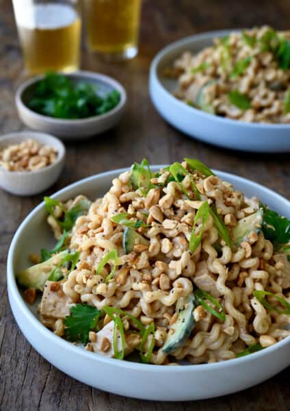 Thai Chicken Pasta Salad in a white bowl garnished with sliced scallions and chopped peanuts.