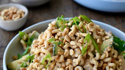 Thai Chicken Pasta Salad in a white bowl garnished with sliced scallions and chopped peanuts.