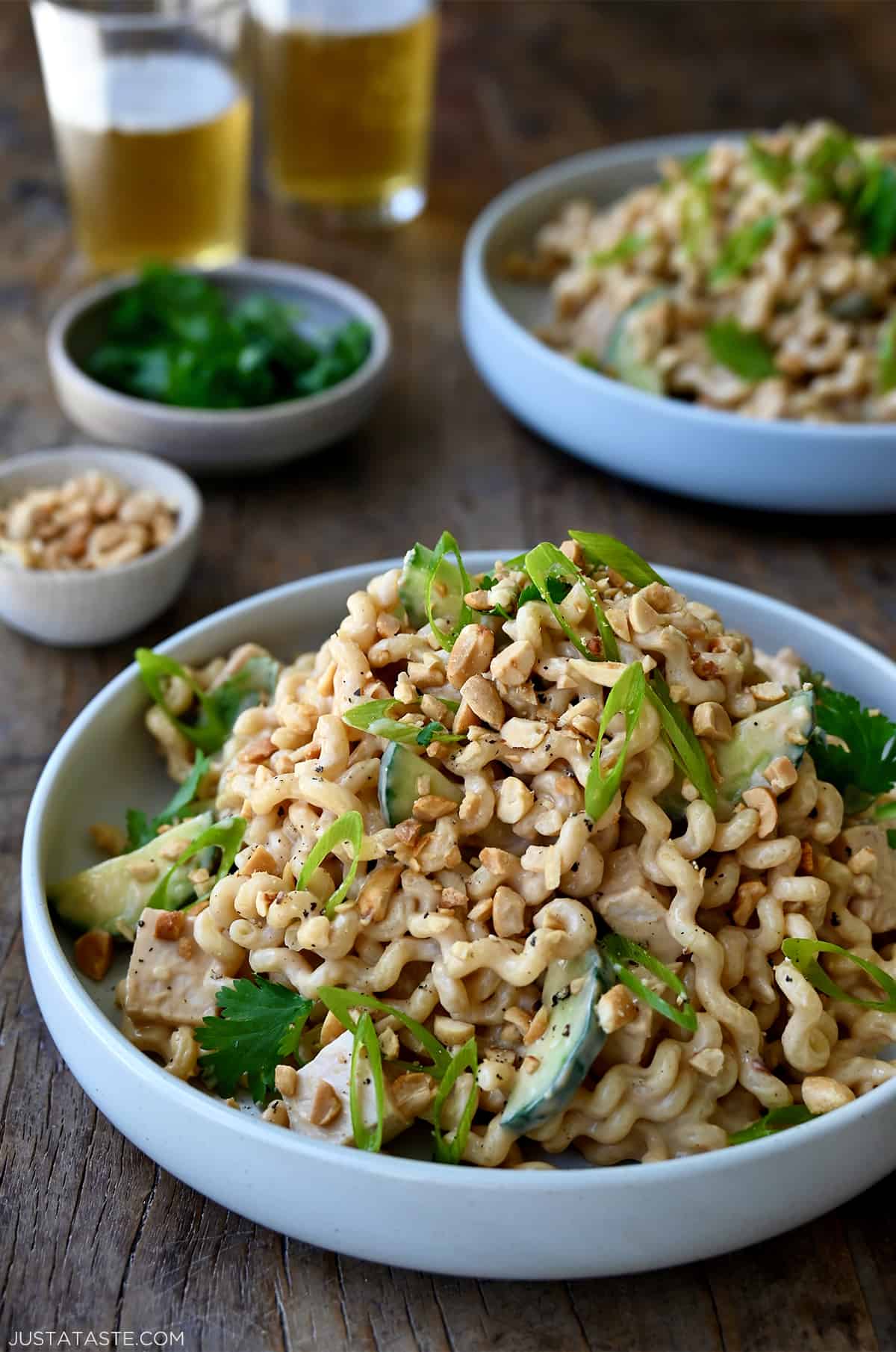 Thai Chicken Pasta Salad in a white bowl garnished with sliced scallions and chopped peanuts.