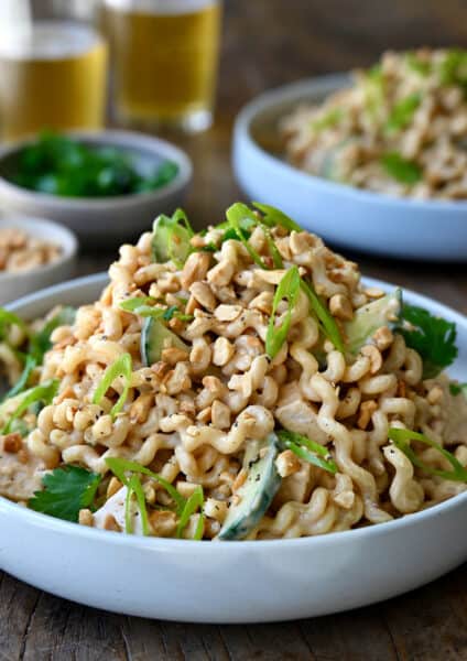 A white dinner bowl containing Thai Chicken Pasta Salad with sliced cucumbers and scallions, and shredded rotisserie chicken.