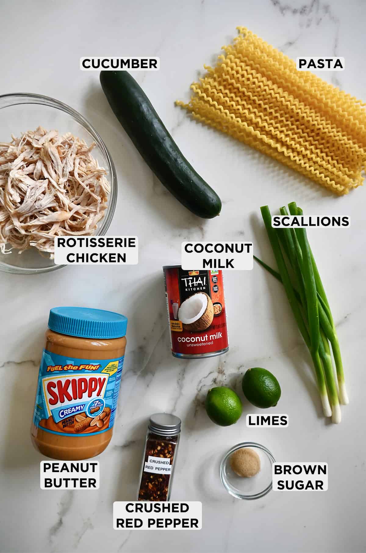 All the ingredients needed to make Thai Pasta Salad, including long pasta noodles, scallions, limes, brown sugar, crushed red pepper flakes, peanut butter, coconut milk and chicken.