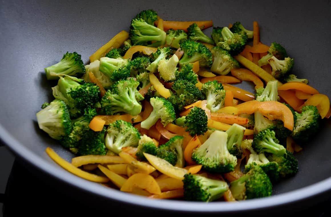 A wok containing yellow and orange pepper strips, and broccoli florets