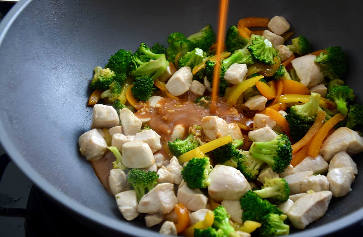 Sauce being poured over vegetables in a wok