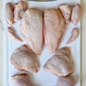 A whole chicken cut into 12 pieces on a cutting board.