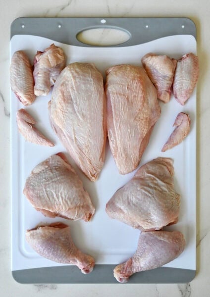 A whole chicken cut into 12 pieces on a cutting board.