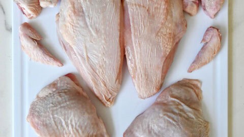 A whole chicken cut into 12 pieces on a cutting board.