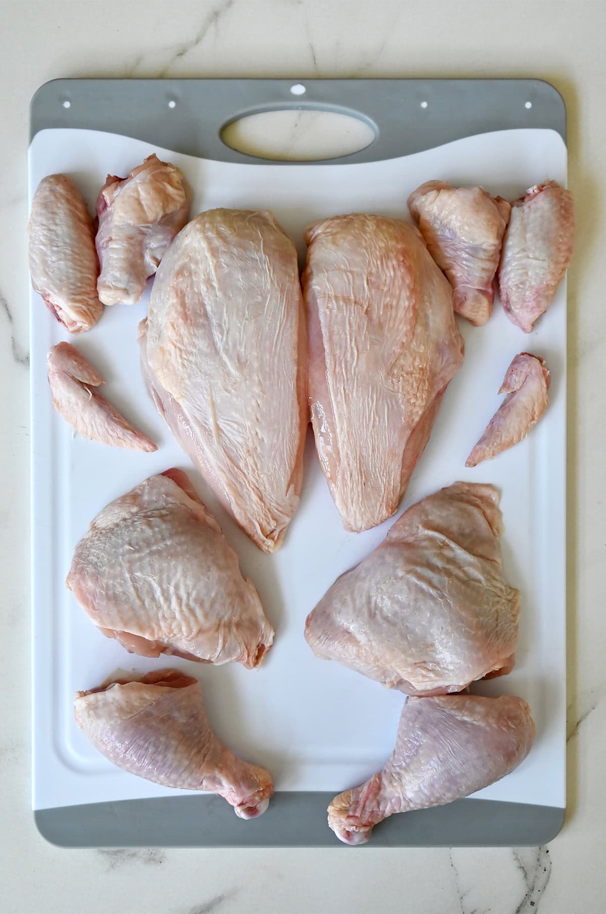 A whole chicken cut into 12 pieces on a cutting board.
