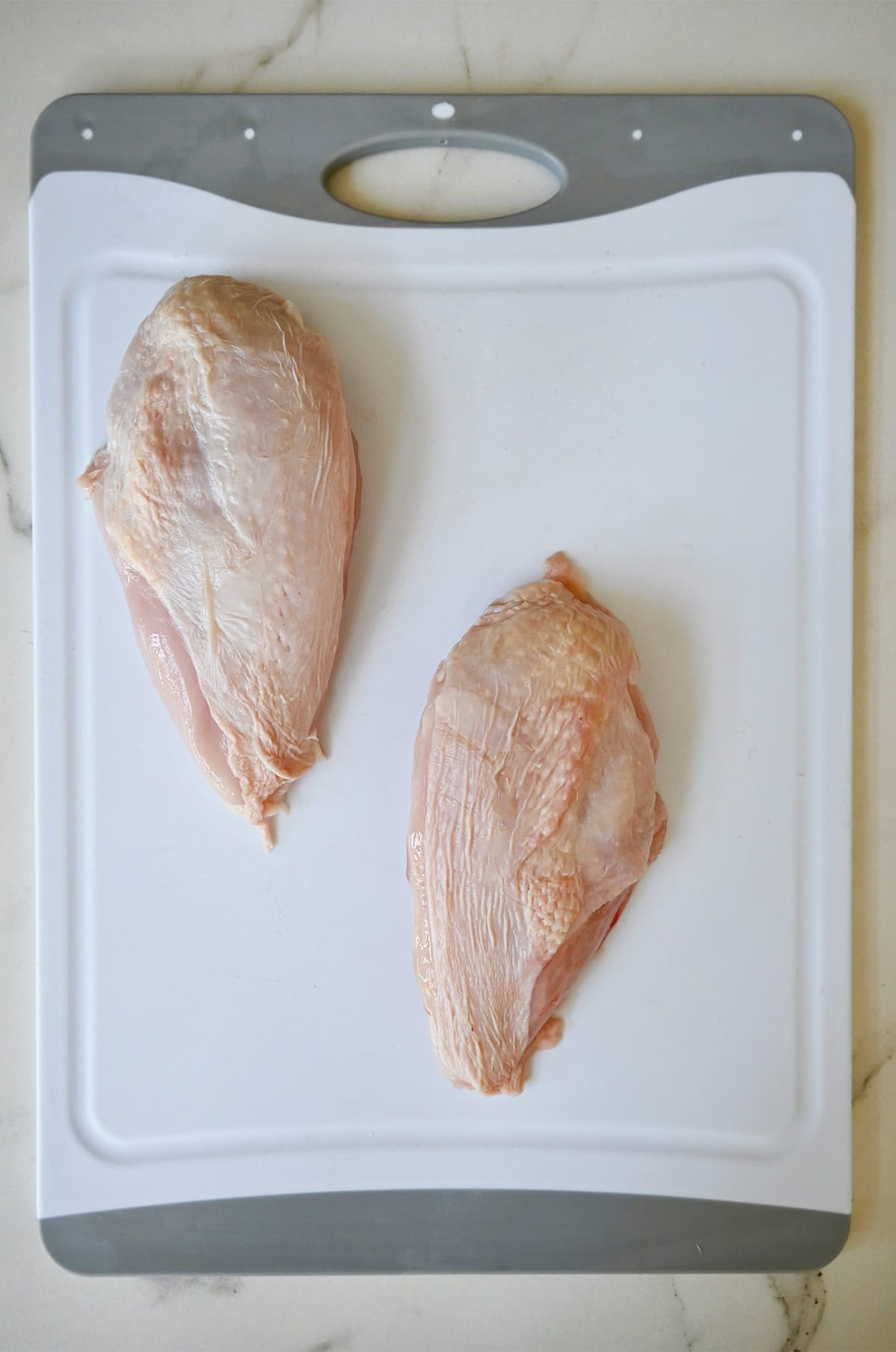 Two chicken breasts on a cutting board.