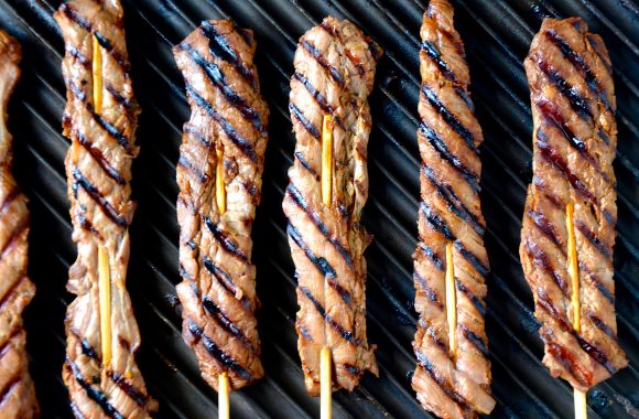 A grill pan with beef skewers on sticks