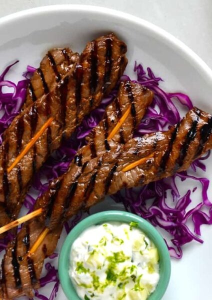 A white plate containing purple shredded cabbage and beef kabobs on skewers
