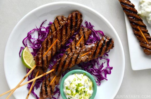 A white plate containing purple shredded cabbage and beef kabobs on skewers