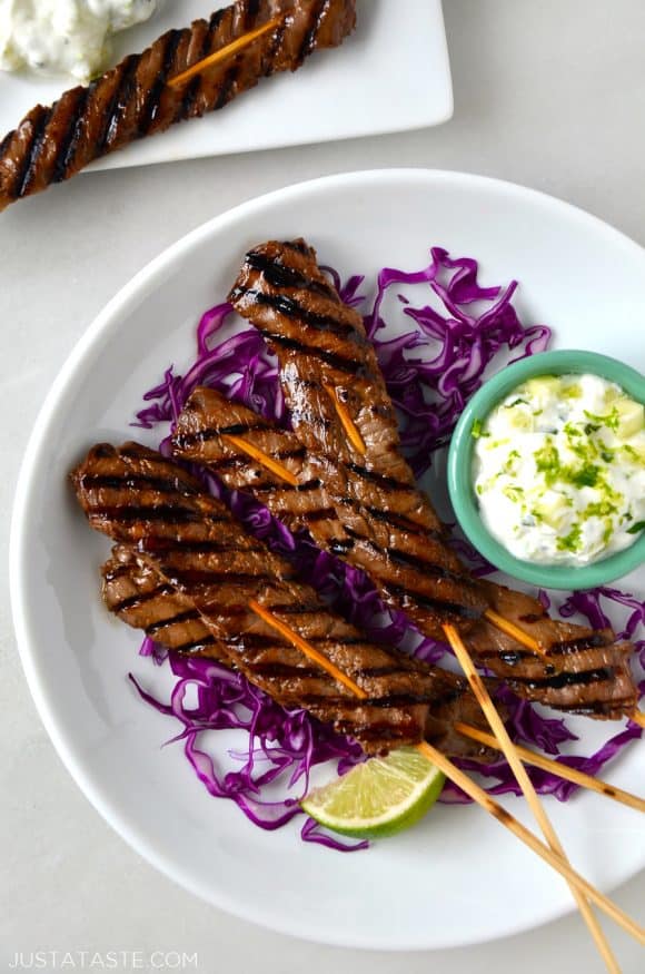 A circular white plate with purple cabbage, beef skewers and yogurt dip