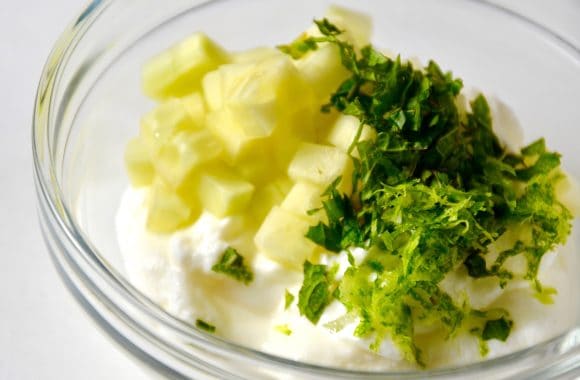 A clear bowl containing yogurt, diced cucumbers and lime zest