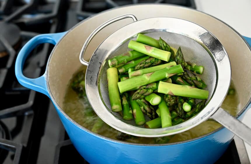 Blanched asparagus in a strainer over a large pot filled with water