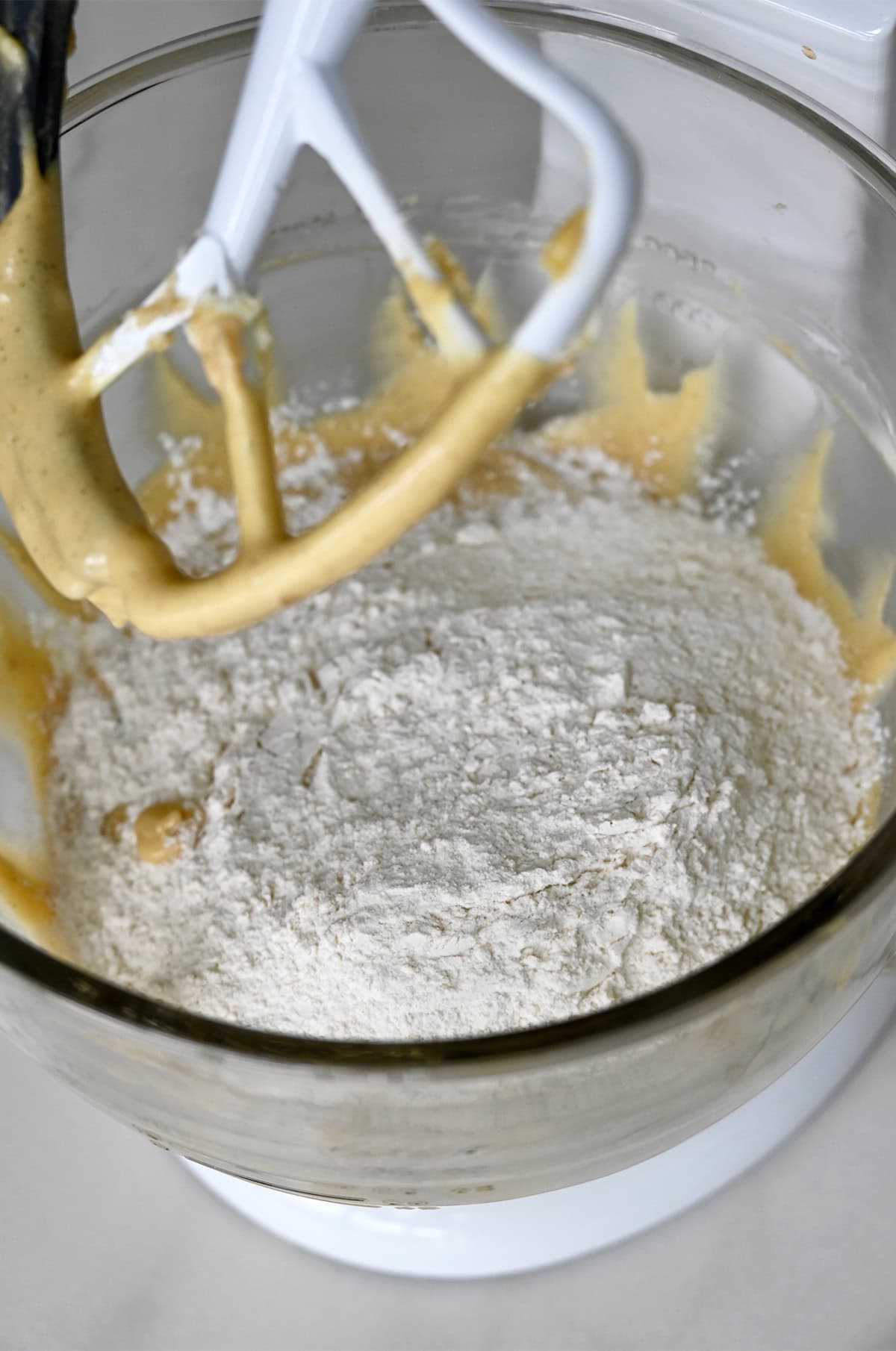 A flour mixture atop creamed wet ingredients in the bowl of a stand mixture.