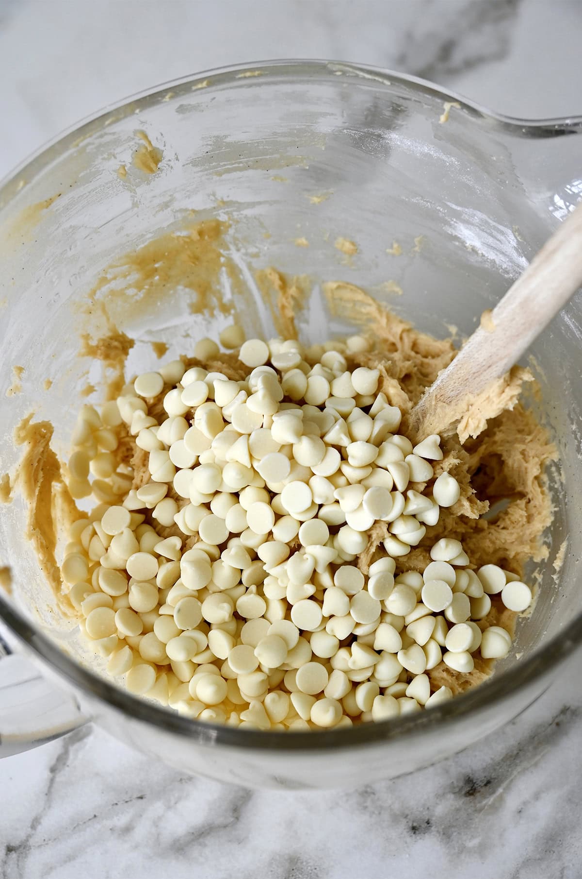 White chocolate chips atop cookie dough in a glass bowl.