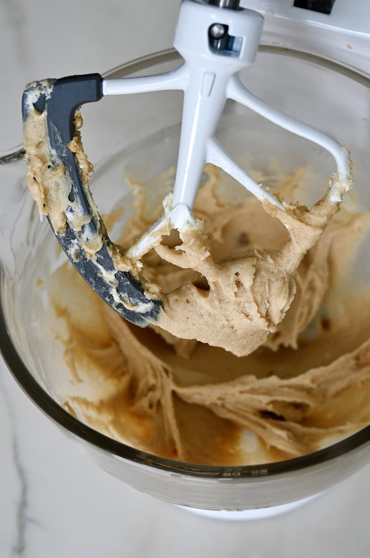 Creamed butter, cream cheese, sugar, light brown sugar and vanilla extract covering the paddle attachment of a stand mixer.
